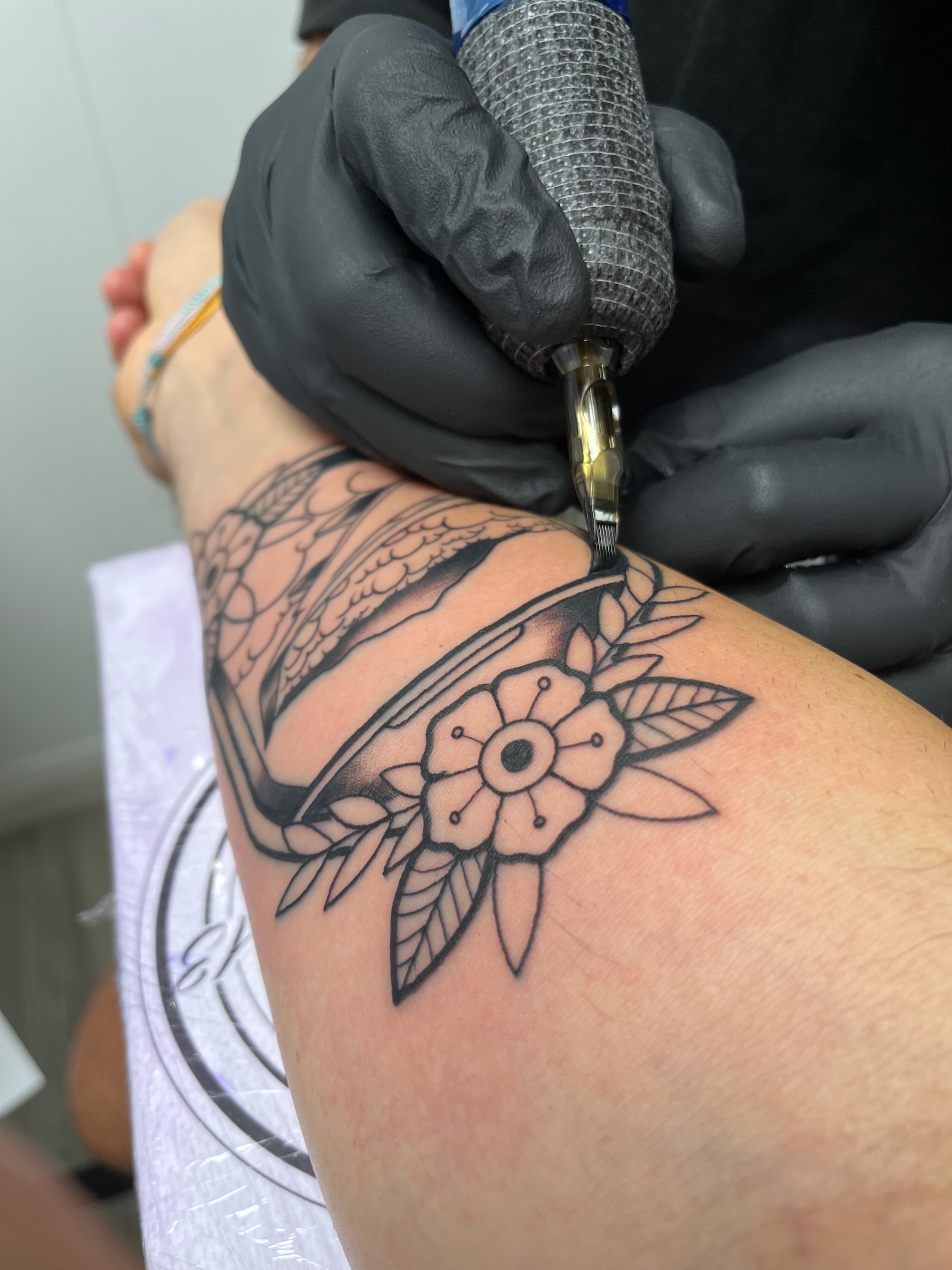 Primer plano de la mano del tatuador, con guantes negros y pistola sobre la piel, en pleno trabajo trazando el dibujo sobre mi brazo.